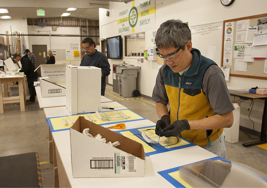 Kaiser Permanente Cabinet Maker David Li, foreground, puts together disposable face shields for Northern California clinicians at a carpentry shop in Berkeley.  (Photo by Doug Oakley)