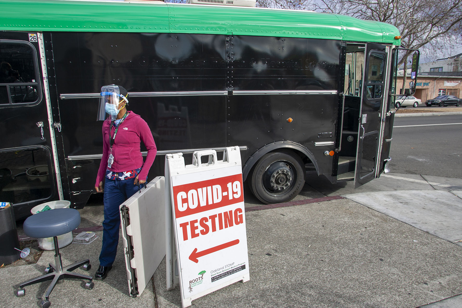 Maggie McNair, RN, of Roots Community Health Center, sets up a COVID-19 testing station on the sidewalk in East Oakland near the organization's mobile health clinic bus.