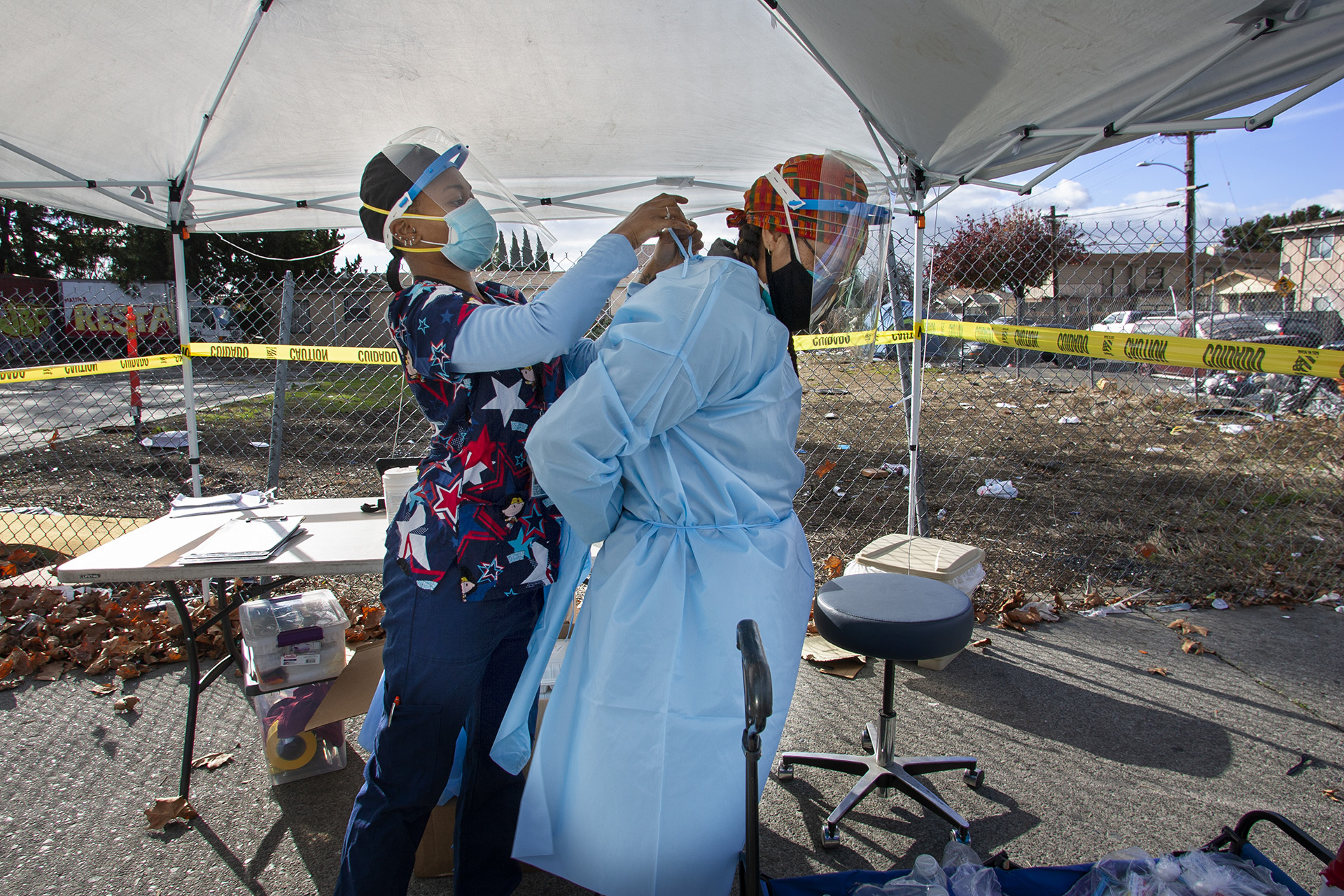 Maggie McNair, RN, at left, helps Danielle Williams, MD, at right into personal protective gear at a COVID-19 testing station in East Oakland as part of Roots Community Health Center's homeless outreach program.